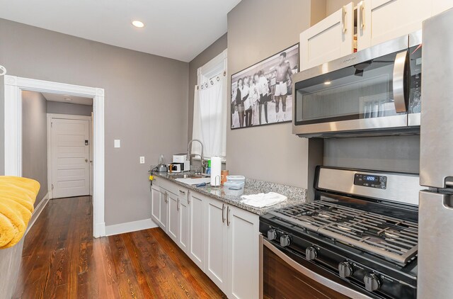 kitchen with light stone counters, dark hardwood / wood-style floors, stainless steel appliances, and white cabinets