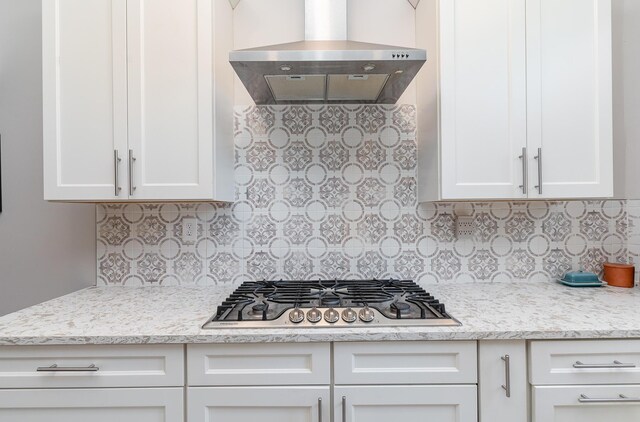 kitchen featuring stainless steel gas stovetop, wall chimney range hood, backsplash, light stone countertops, and white cabinetry