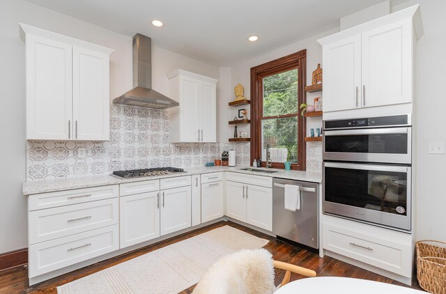 kitchen featuring appliances with stainless steel finishes, decorative backsplash, white cabinets, and wall chimney range hood