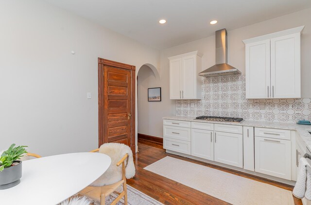 kitchen featuring light hardwood / wood-style flooring, stainless steel gas stovetop, tasteful backsplash, wall chimney range hood, and white cabinets