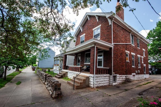 view of front of home with covered porch, a chimney, and brick siding