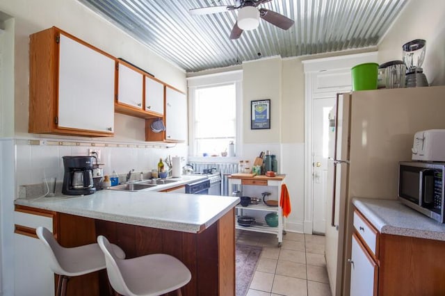 kitchen with light tile patterned floors, light countertops, stainless steel microwave, a sink, and a peninsula