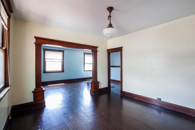 spare room featuring decorative columns, baseboards, and wood finished floors