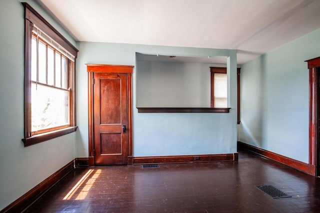 empty room with wood-type flooring, visible vents, and baseboards