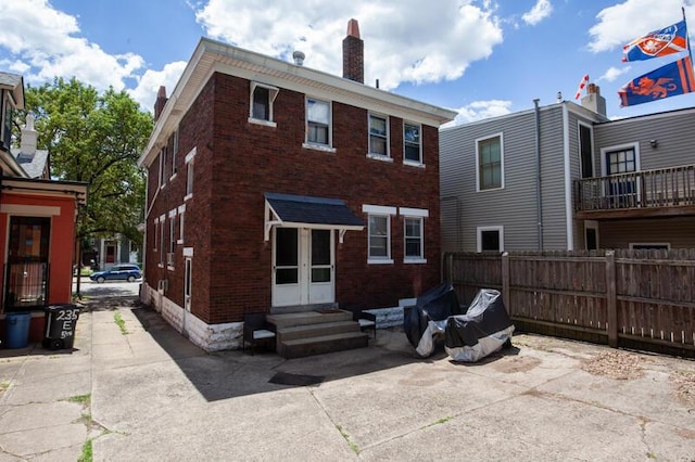 rear view of house with entry steps, brick siding, a chimney, and fence