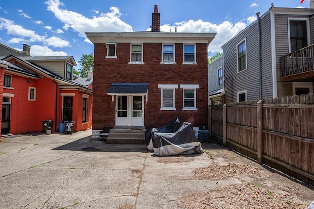 back of house featuring entry steps, brick siding, a chimney, and fence