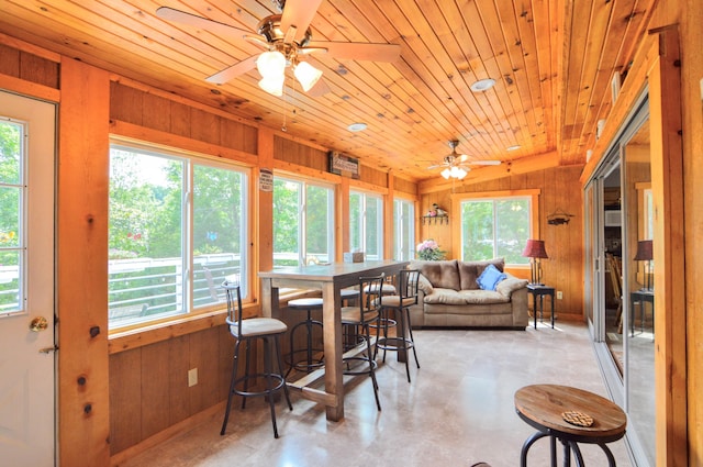 dining area with ceiling fan, a wealth of natural light, wooden ceiling, and wooden walls