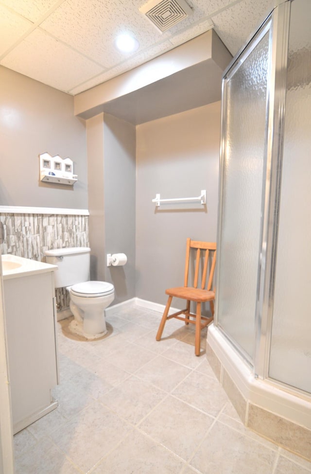 bathroom with a paneled ceiling, vanity, walk in shower, toilet, and tile patterned floors