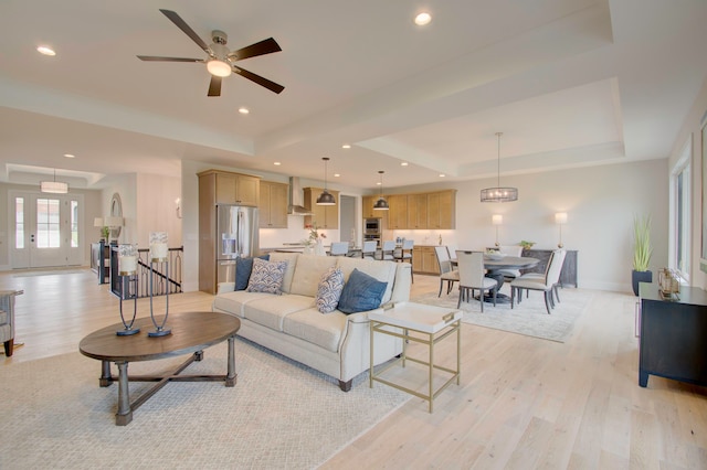 living room with a tray ceiling, light hardwood / wood-style floors, and ceiling fan