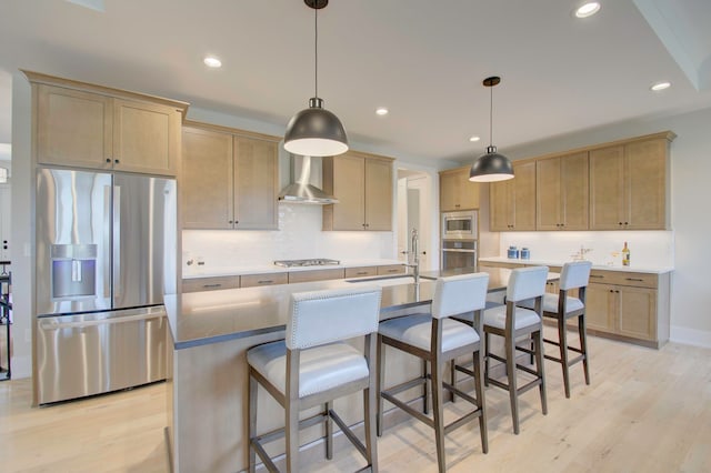 kitchen featuring light hardwood / wood-style floors, an island with sink, wall chimney exhaust hood, stainless steel appliances, and sink