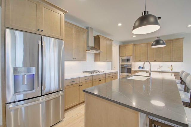 kitchen featuring hanging light fixtures, light hardwood / wood-style flooring, wall chimney exhaust hood, appliances with stainless steel finishes, and a breakfast bar