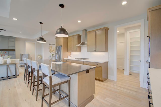 kitchen with light wood-type flooring, a center island with sink, wall chimney range hood, and sink