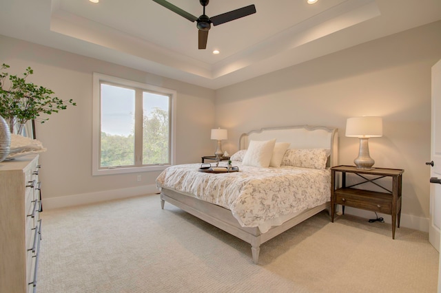 bedroom with light carpet, a tray ceiling, and ceiling fan