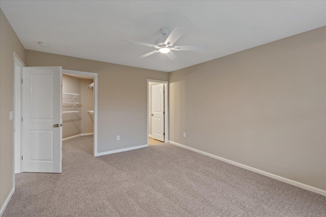 unfurnished bedroom featuring a walk in closet, light carpet, ceiling fan, and a closet