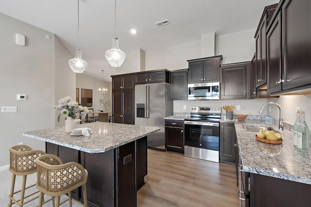 kitchen with appliances with stainless steel finishes, pendant lighting, sink, a center island, and light hardwood / wood-style flooring