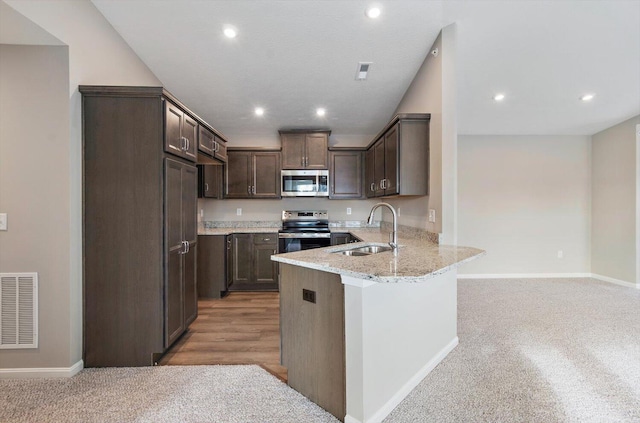 kitchen featuring appliances with stainless steel finishes, sink, dark brown cabinetry, kitchen peninsula, and light stone countertops