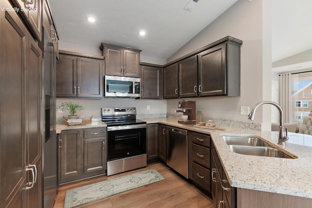 kitchen featuring light stone counters, lofted ceiling, stainless steel appliances, and sink