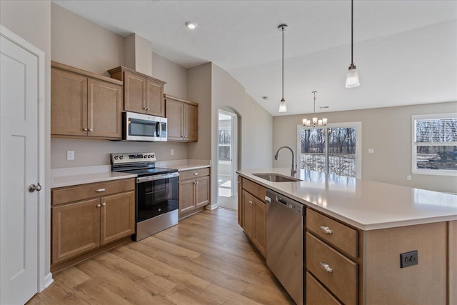 kitchen featuring appliances with stainless steel finishes, an island with sink, sink, hanging light fixtures, and light hardwood / wood-style floors