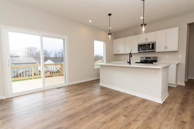 kitchen featuring pendant lighting, stainless steel appliances, white cabinetry, and a center island with sink