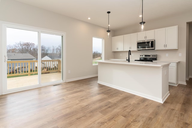 kitchen with white cabinetry, hanging light fixtures, a center island with sink, appliances with stainless steel finishes, and light wood-type flooring