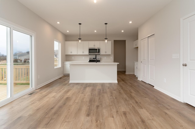 kitchen with a kitchen island with sink, sink, light hardwood / wood-style floors, white cabinetry, and hanging light fixtures