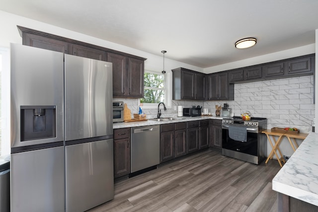 kitchen featuring appliances with stainless steel finishes, hanging light fixtures, hardwood / wood-style flooring, decorative backsplash, and dark brown cabinetry