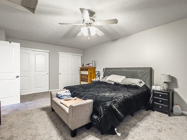 bedroom featuring a textured ceiling, carpet flooring, two closets, and ceiling fan