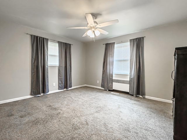 carpeted empty room with ceiling fan, plenty of natural light, and radiator heating unit