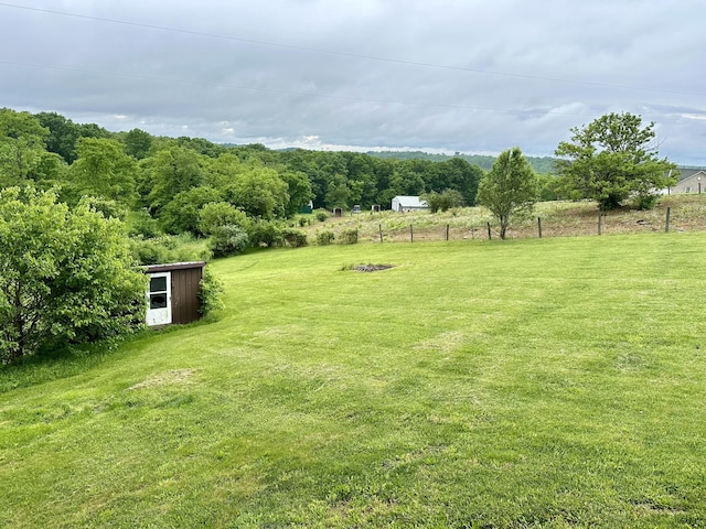 view of yard featuring a storage shed, fence, an outdoor structure, and a rural view