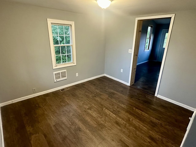 spare room featuring dark wood-style flooring, visible vents, and baseboards