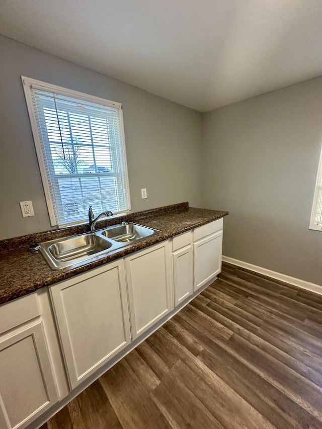 kitchen with dark wood-style floors, white cabinets, a sink, dark stone counters, and baseboards