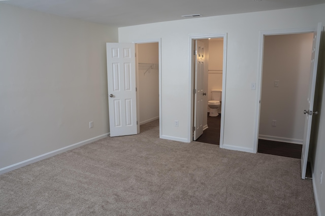 unfurnished bedroom featuring a walk in closet, ensuite bathroom, light colored carpet, and a closet