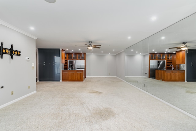 unfurnished living room featuring light colored carpet, sink, crown molding, and ceiling fan