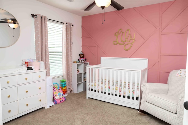 bedroom featuring light colored carpet, a nursery area, and ceiling fan