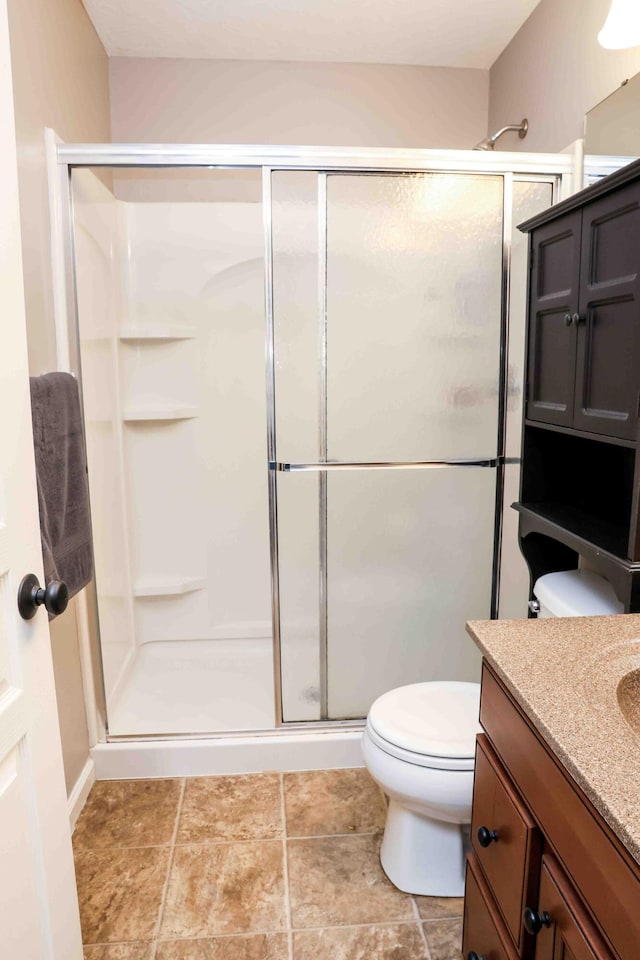 bathroom featuring tile patterned floors, a shower with door, vanity, and toilet