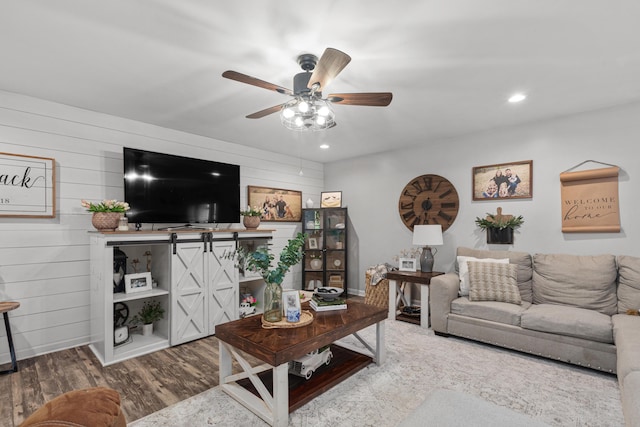 living room featuring wooden walls, a ceiling fan, wood finished floors, and recessed lighting