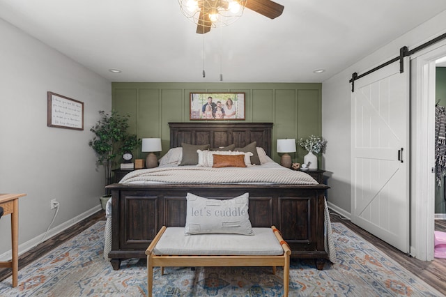 bedroom with a barn door, baseboards, a decorative wall, and wood finished floors