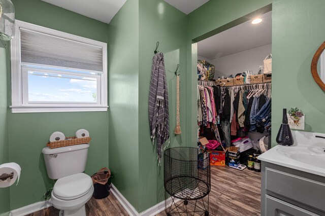 full bath with a spacious closet, toilet, vanity, wood finished floors, and baseboards