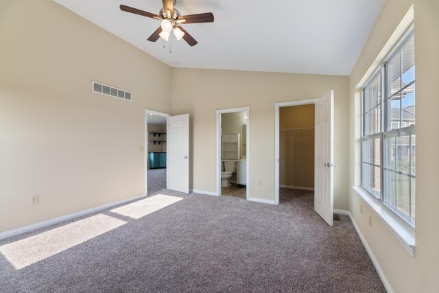 unfurnished bedroom featuring lofted ceiling, ceiling fan, a walk in closet, ensuite bathroom, and light colored carpet