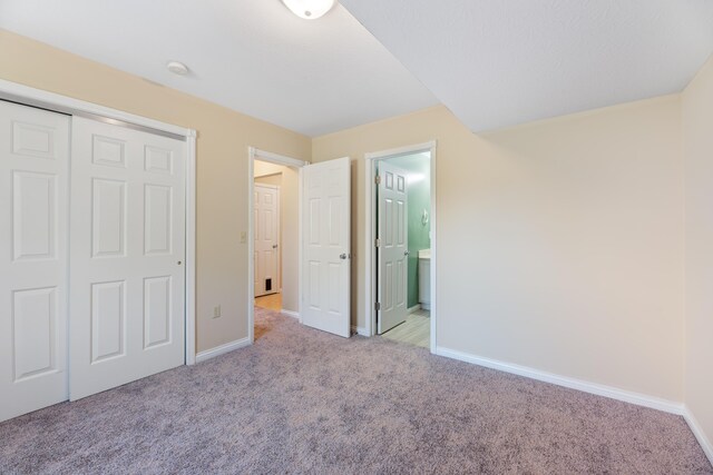 unfurnished bedroom featuring light carpet, a closet, and ensuite bath