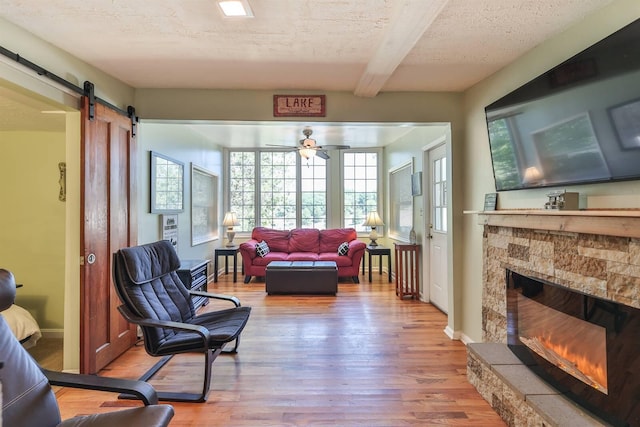 living room featuring a textured ceiling, hardwood / wood-style floors, a stone fireplace, a barn door, and ceiling fan