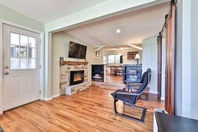 living room with lofted ceiling with beams, a healthy amount of sunlight, hardwood / wood-style floors, and a stone fireplace