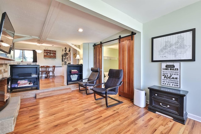 living area with a barn door, light wood-style floors, baseboards, and beamed ceiling