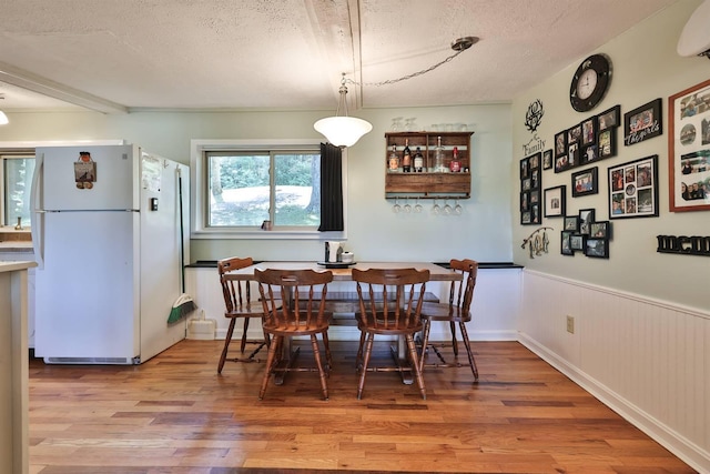 dining space featuring a wall mounted AC, wood-type flooring, wooden walls, and a textured ceiling