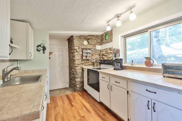kitchen with white cabinets, a sink, a textured ceiling, tile counters, and white range with electric stovetop