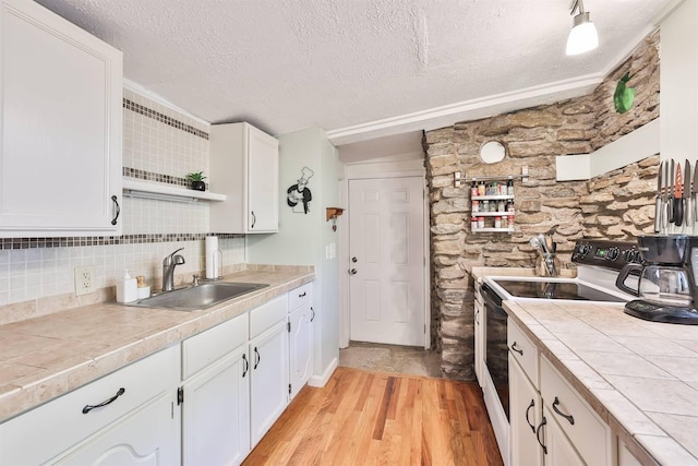 kitchen featuring white electric stove, a sink, a textured ceiling, light wood-type flooring, and tile counters