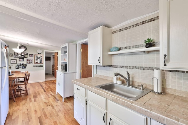 kitchen featuring pendant lighting, backsplash, sink, white cabinetry, and light wood-type flooring