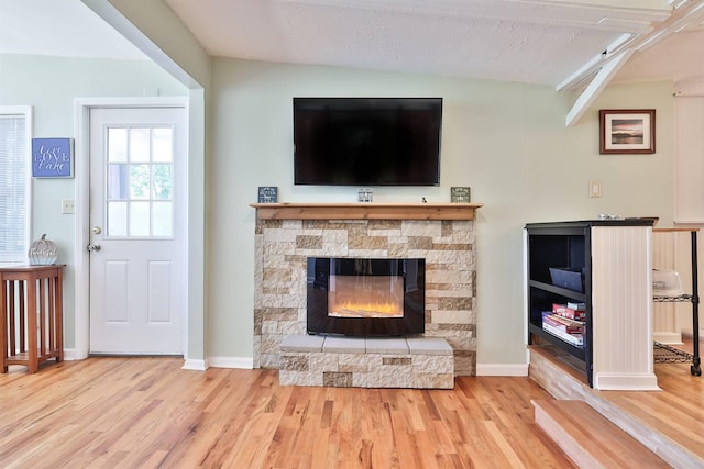living room with beamed ceiling, wood finished floors, baseboards, and a stone fireplace
