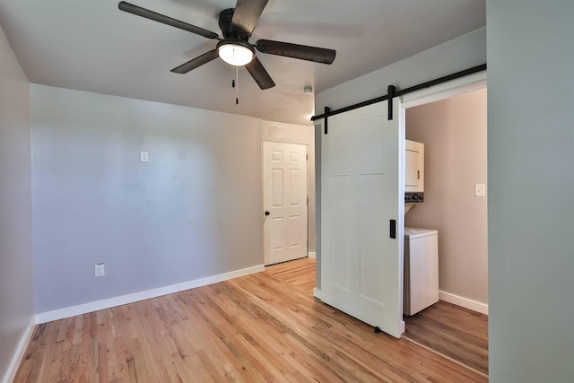 unfurnished bedroom with ensuite bathroom, ceiling fan, a barn door, and light hardwood / wood-style floors