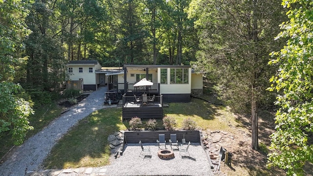 rear view of house with a fire pit, a view of trees, a deck, and a lawn